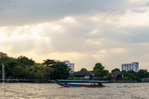 Принти на полотні A long tail boat sailing on Chaophraya River, Thailand at sunset with some moder