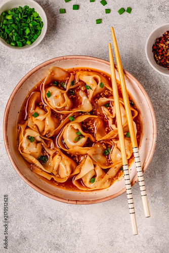 Wontons are placed in a bowl with spicy sauce.