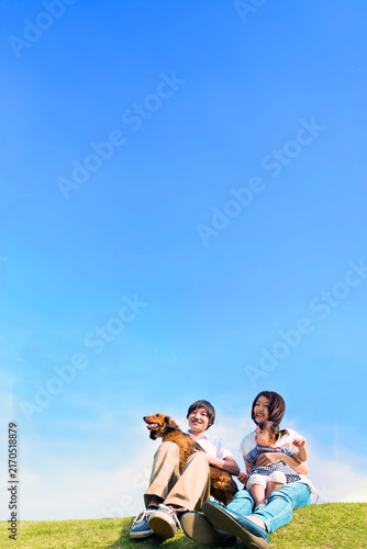 青空を背景に犬のペットと芝に座る幼い女の子と幸せな家族