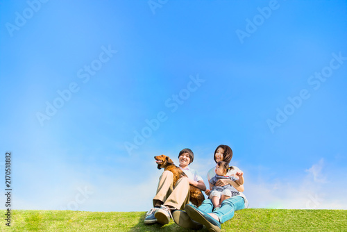 青空を背景に犬のペットと芝に座る幼い女の子と幸せな家族