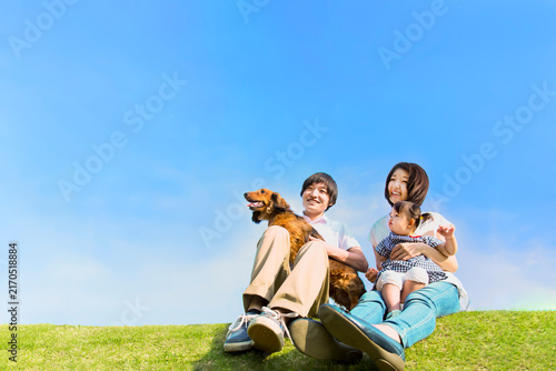 青空を背景に犬のペットと芝に座る幼い女の子と幸せな家族