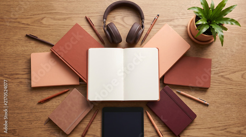 Creative desk with spiral notebook, books, headphones, tablet, and plant in symmetrical layout.