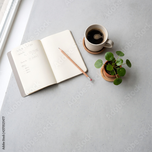 A clean white desk with a to-do list notebook, pencil, coffee cup, and succulent plant bathed in soft morning light.