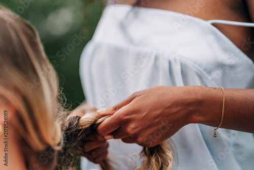 Woman carefully braiding another persons long blonde hair