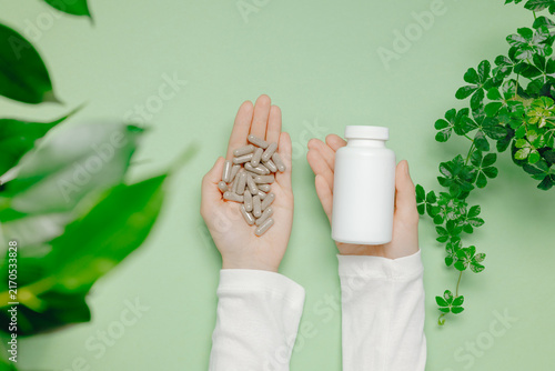 Woman hands with herbal supplement pills with plant leaves top view