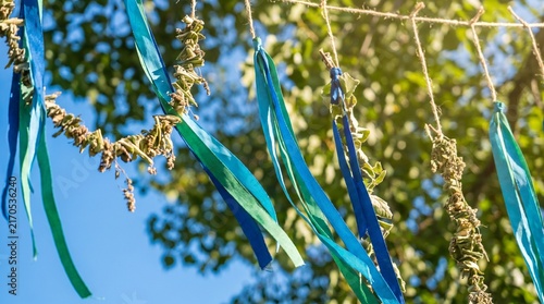Photorealistic close-up of blue and green eco-friendly decorations moving in the breeze, framed by a clear blue sky and green leaves, with soft sunlight and elegant minimal Clean Air Day styling