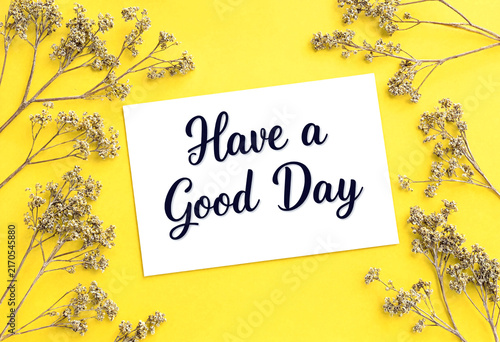Bright yellow background with white card saying have a good day surrounded by delicate flowers