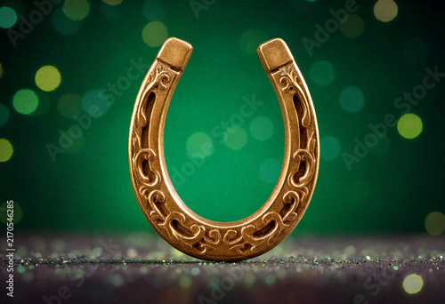 Decorative golden horseshoe with intricate patterns and elegant design on green bokeh lights background