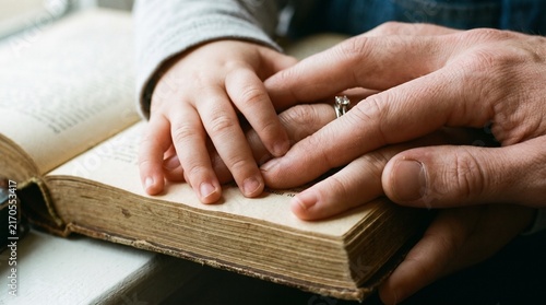 A child and an adult touching an old book together.