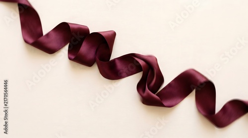 Maroon burgundy satin ribbon curled cream background