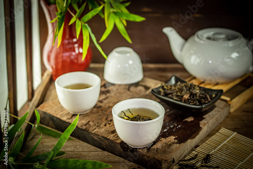Traditional Asian Oolong tea served in white ceramic cups on an antique wooden table with loose leaves and bamboo, creating a peaceful and refined atmosphere for health wellness and relaxation.