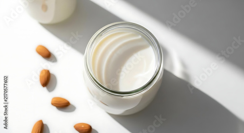 A glass jar filled with creamy almond milk placed on a white surface with nuts