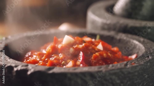 Fiery Salsa Preparation: Freshly prepared salsa, vibrant red with chunks of tomato and garlic, steams gently in a rustic stone mortar, hinting at its spicy flavor and homemade goodness.