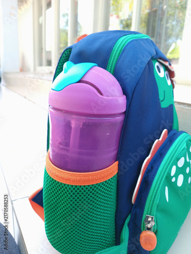 Child's blue dinosaur backpack with purple water bottle in side mesh pocket for school or outdoor activity