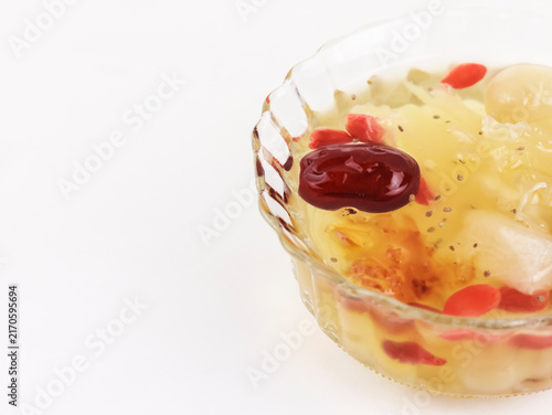 A bowl of traditional Asian sweet dessert soup, featuring snow fungus, red dates, goji berries, and chia seeds in a clear glass bowl against a white background. 