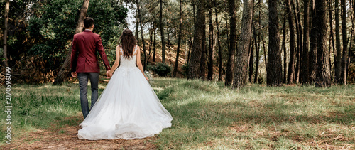 Back view of bride and groom walking in forest