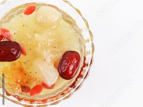 A top-down close-up studio shot of a traditional Asian sweet dessert soup served in a clear glass bowl against a clean white background, with ample copy space on the right.