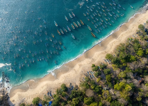 Aerial view of Papuma Beach with numerous traditional fishing boats anchored in the turquoise waters along the sandy coastline and lush green trees Jember, East Java, Indonesia.