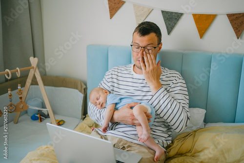 Fotografie Tired father working from home with sleeping newborn, experiencing parental burn