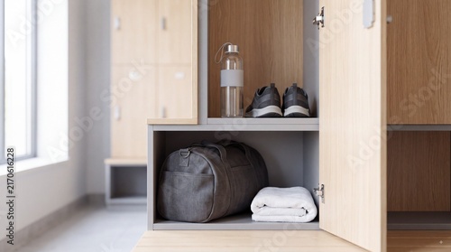 Locker room storage with gray duffel bag, rolled white towel, water bottle, and athletic shoes on wooden shelf in modern fitness facility