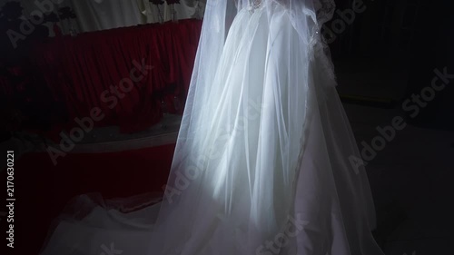 Illuminated bridal gown skirt and veil under soft directional spotlight in dim dressing area, with wedding, dress, veil, tulle detail, showing lace, fabric,skirt,gown context