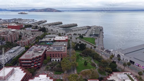 Overcast aerial view revealing the iconic Alcatraz Island, San Francisco Bay, and the urban waterfront architecture of the Embarcadero, including its historic piers and surrounding city buildings