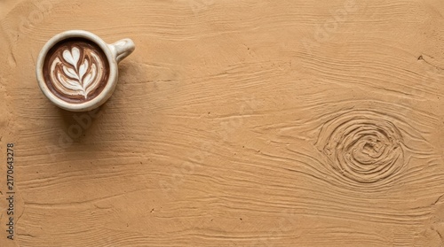 Latte cup on textured tan clay surface.