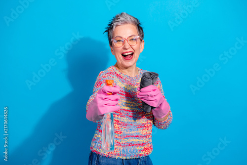 Obraz na płótnie Cheerful senior woman cleaning with spray bottle and cloth wearing pink rubber g