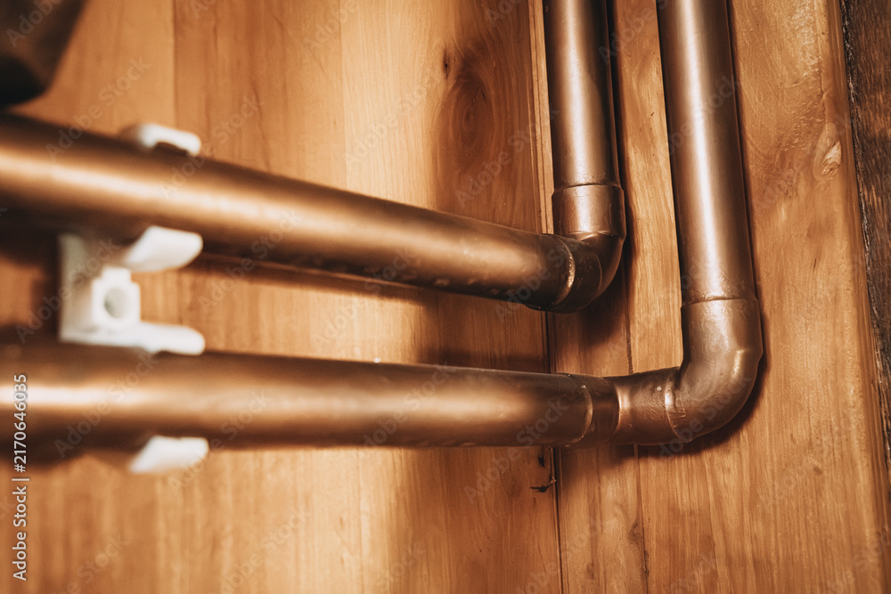 Naklejka premium Close-up angled view of copper water pipes with elbow fittings mounted on a wooden wall panel. Plumbing concept.