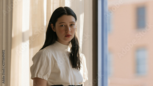 Young Woman Posing Thoughtfully By A Window With Natural Light In A Modern Indoor Setting