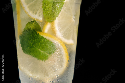 A horizontal macro close-up shot of a frosty glass filled with cold lemonade, ice, lemon slices, and fresh mint leaves for commercial beverage branding and summer advertising campaigns.