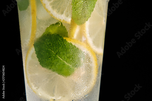 A horizontal macro close-up shot of a frosty glass filled with cold lemonade, ice, lemon slices, and fresh mint leaves for commercial beverage branding and summer advertising campaigns.