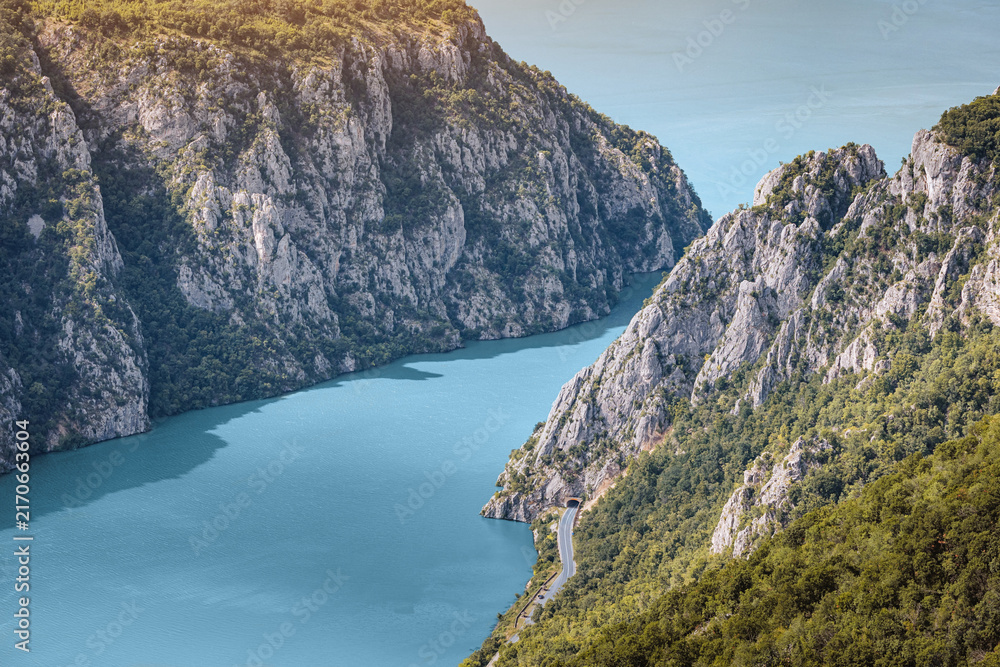 Fototapeta premium Danube River flowing through a deep gorge with steep, forested cliffs and a road following the winding banks in summer