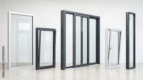 modern aluminum window and door frames displayed in bright white showroom interior on concrete floor, including fixed window, tilt and turn windows in white and anthracite, large lift and slide slidin