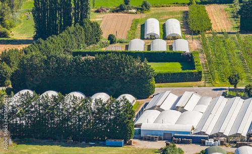 Aerial view of a large horticultural greenhouse complex and plant nursery surrounded by agricultural fields and tree lines in Le Pouzin, Auvergne-Rhone-Alpes, France.