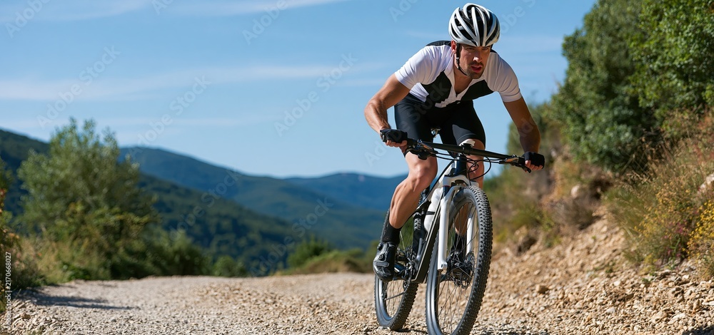 Naklejka premium Male cyclist climbing a mountain trail with determination, set against a vivid natural landscape.