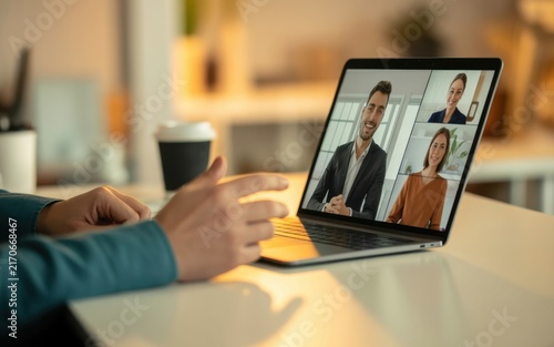 Business team having a virtual conference meeting on laptop screen while working from home office desk with coffee cup in the blurred background setting