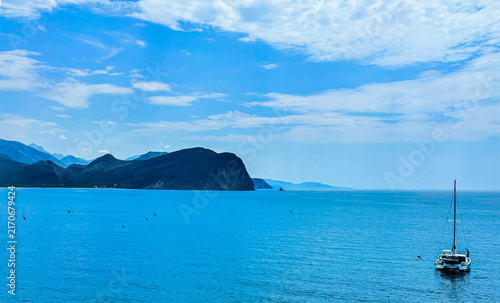 Blue seascape with a yacht and with coastal cliffs and blue sky clouds in background