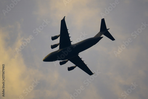 Dark silhouette of a military airplane flying under light blue sky clouds