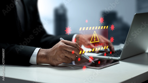 Konstfotografi Businessman working on a laptop and tablet with a holographic virus alert and malware warning hologram floating above