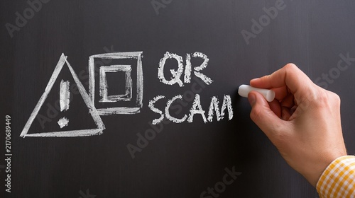 Human hand adding chalk detail to a QR scam sign with matrix barcode and warning triangle on blackboard, ideal for cyber fraud, digital safety and consumer education.