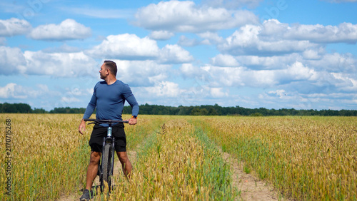 Canvastavla Mid adult sportsman on a bicycle stopping during a cross-country route in a vast wheat field, taking a deep breath and stretching with hands overhead
