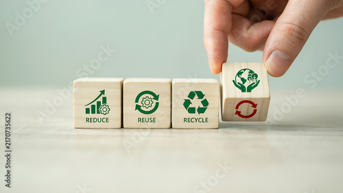 Hand placing sustainability block with recycle symbol on reduce reuse recycle wooden blocks
