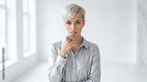 Confident young woman with platinum blonde pixie cut posing in metallic silver shirt
