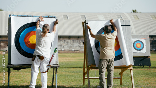 Konstfotografi Two mature men replacing paper targets on archery stands outdoors, preparing for