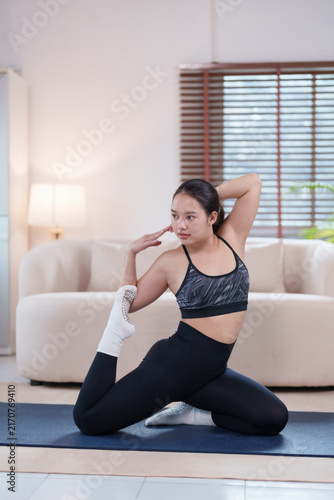 Fotografie Young Asian woman performing a yoga pose, stretching her leg and arm on a mat at