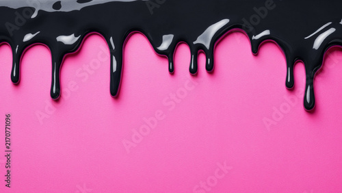 thick black glossy paint dripping down on pink paper background creating a bold abstract pattern