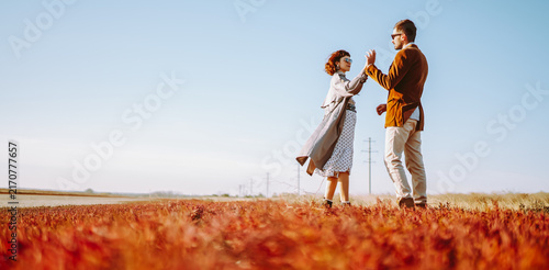 Bild auf Leinwand Stylish couple walks through a sunny field surrounded by red grass