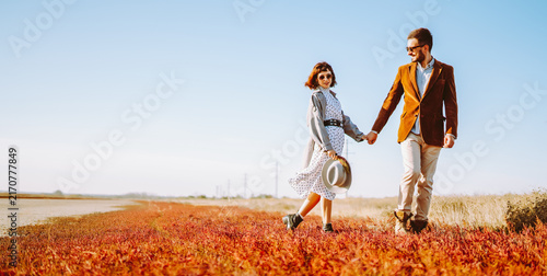 Konstfotografi Stylish couple walks through a sunny field surrounded by red grass
