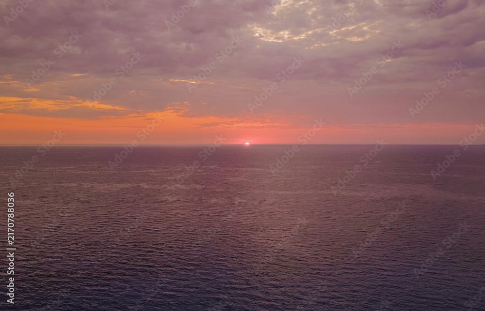 Fototapeta premium Aerial view of vibrant purple and orange sunset over quiet open Ionian sea horizon with dramatic cloudy sky in Lefkada island Greece horizontal stock photo